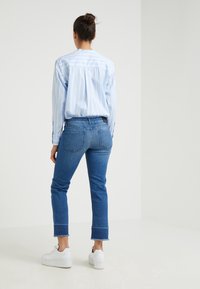 Camisa de botones a rayas azul claro con un corte relajado, combinada con jeans oscuros ajustados con dobladillo deshilachado y zapatillas blancas.