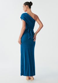 En-ærmet, figursyet kjole i rigblåt stof med en blød tekstur. Har et bindebånd ved taljen og en gulvlængde silhuet.