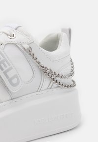 Sneakers à plateforme blancs avec détail chaîne argentée, panneaux en mesh et cuir, et logo embossé "KARL LAGERFELD" sur la semelle et le côté.