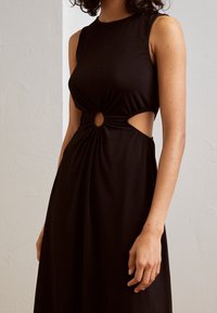 Robe noire sans manches avec une découpe à la taille, ornée de détails froncés et d'un accent circulaire, fabriquée dans un tissu doux et lisse.