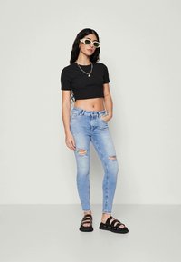 Black cropped t-shirt, light blue distressed jeans, and black strappy sandals. Accessories include green sunglasses and a silver chain necklace.