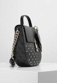 Sac à main noir à forme structurée, matériau texturé, design clouté, ferrures argentées et bandoulière chaîne amovible.