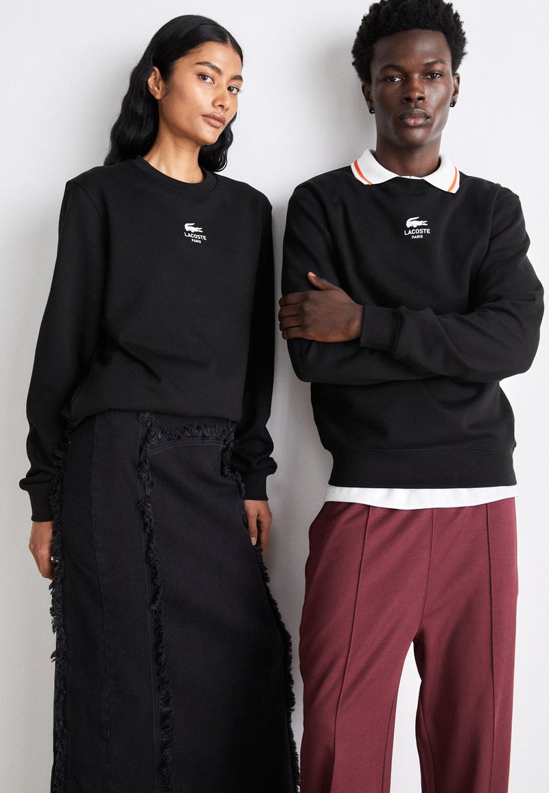 Sweatshirts noirs avec logo sur la poitrine, associés à une jupe noire à franges et un pantalon bordeaux ; présentation de textures et couleurs variées.