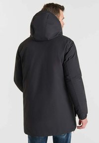 Cappotto isolato nero con cappuccio, caratterizzato da un tessuto esterno liscio e un orlo posteriore leggermente più lungo. Nessun hardware o motivo visibile.
