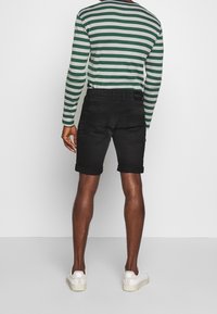 Shorts in denim nero con risvolti, abbinati a una camicia a maniche lunghe a righe verde e bianca. Calzature sono scarpe da ginnastica bianche.