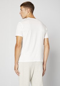 Vit kortärmad skjorta, mjukt bomullstyg, rundad halsringning, åtsittande vid axlarna, matchad med ljusgrå sweatpants, sett bakifrån.