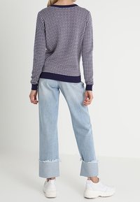 Svetr s námořnickým vzorem a dlouhými rukávy, zakončený žebrovanými manžetami; nošený s širokými modrými džíny s roztrhanými lemy a bílými teniskami.