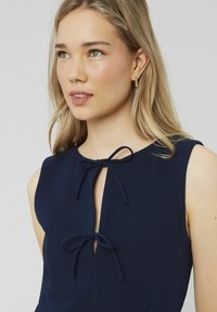 Robe marine avec un col en trou de serrure, dotée d'une fermeture à nouer et d'un design sans manches. Tissu lisse et détails de couture subtils.