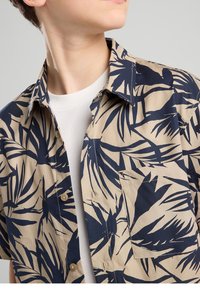 Camisa de manga corta con botones en beige con diseño de hojas en azul marino, con cuello puntiagudo y bolsillo en el pecho, confeccionada en tela de algodón ligera.