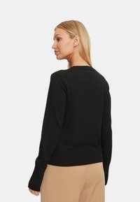 Maglione nero a maglia con una vestibilità rilassata, polsini e orlo ribattuti. Texture liscia, scollo rotondo e dettaglio di branding minimale sul retro.