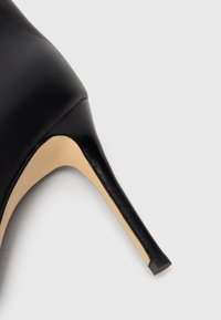 Schwarzer Leder-Pumps mit beiger Sohle und schmalem Stilettostiletto auf weißem Hintergrund.