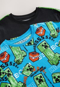 Kurzärmeliges T-Shirt mit blauem Körper, grünen Minecraft-Creeper-Grafiken und schwarzen kurzen Ärmeln sowie einem gerippten Rundhalsausschnitt.