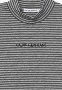 Šedé pruhované tričko z látky s vysokým límcem a logem Calvin Klein Jeans v černé barvě. Textura obsahuje jemné kovové nitě pro třpytivý efekt.