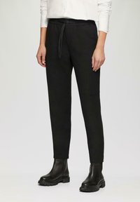 Pantalons noirs à taille élastique avec un cordon de serrage, poches latérales et coupe fuselée, associés à des bottines noires. Texture lisse.