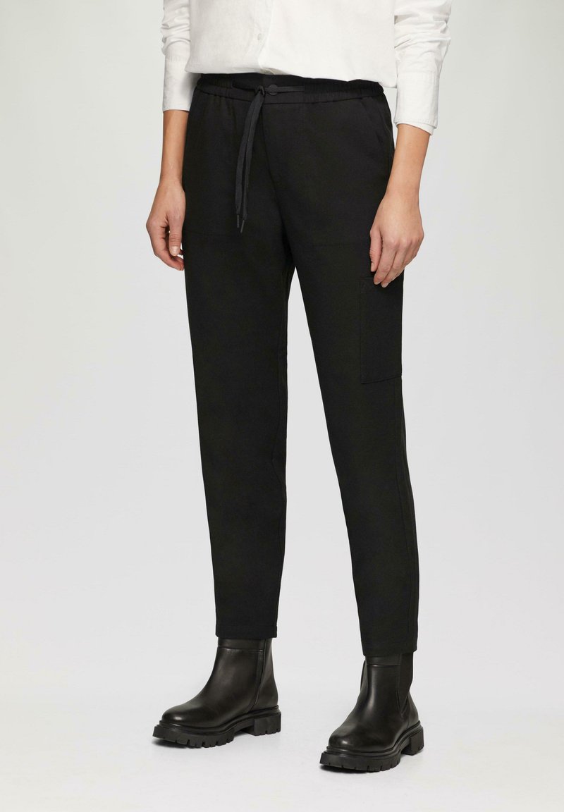 Pantalons noirs à taille élastique avec un cordon de serrage, poches latérales et coupe fuselée, associés à des bottines noires. Texture lisse.