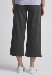 Tmavě šedé kalhoty typu culotte vyrobené z měkké tkaniny, s širokým střihem a hladkým povrchem, doplněné o bílé tenisky.