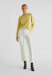Geel gebreide trui met een ronde hals, gecombineerd met witte hoge taille, wijde jeans en donkergrijze enkellaarsjes. Eenvoudig ontwerp en textuur.