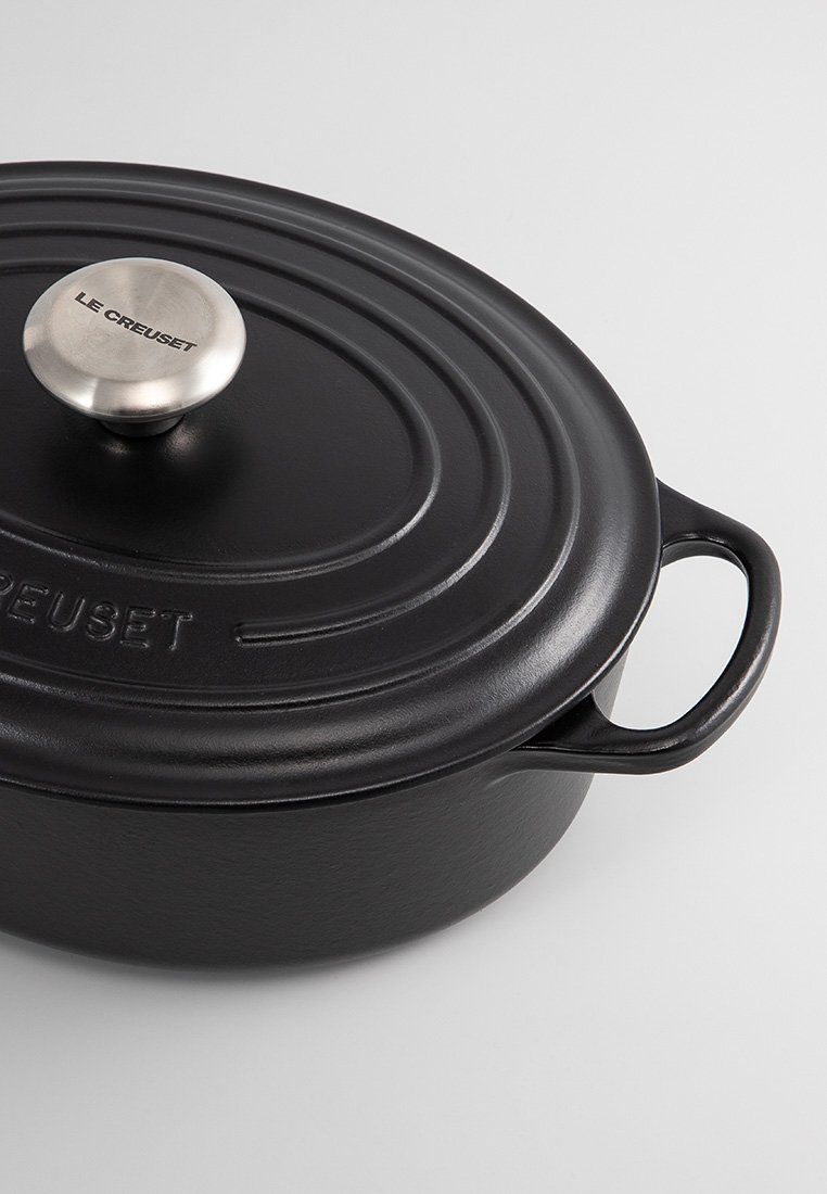 Schwarzer Gusseisen-Bräter mit glatter Oberfläche, gewölbtem Deckel und Edelstahlknopf. Verfügt über zwei seitliche Griffe für einfaches Anheben.