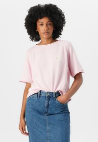 Lyse rosa teksturert kortermet topp med løs passform og rund hals, parret med et høy midje blå denimskjørt. Små logo-detaljer.