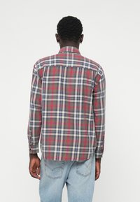 Chemise à carreaux avec un mélange de nuances rouges, bleues et grises, manches longues et ourlet arrondi. Fabriquée en tissu léger avec un col à bouton.