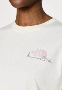 Μπεζ T-shirt με το λογότυπο «THE NORTH FACE» σε ροζ χρώμα, μαζί με γραφικό σκηνής και δέντρου. Στρογγυλή λαιμόκοψη, απαλή υφή βαμβακιού.