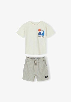 T-shirt à manches courtes blanc cassé avec un graphisme de voilier bleu et du texte, associé à un short beige à rayures grises avec cordon de serrage et poches avant.