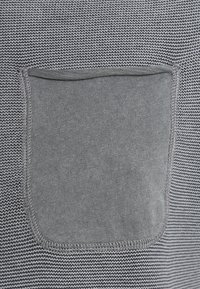 Grauer Strickstoff mit horizontalen Streifen, versehen mit einer einfarbigen grauen aufgesetzten Tasche. Die Textur ist glatt, mit sichtbaren Nähten und Stickdetails.
