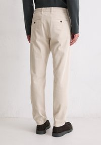 Pantalon en velours côtelé beige à coupe droite, avec poches arrière, texture côtelée subtile, et porté avec des chaussures foncées.