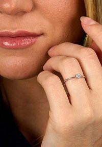 Silberring mit einem herzförmigen, klaren Edelstein, schmale Fassung, glatte Textur. Am Zeigefinger getragen, zeigt ein zartes Design.