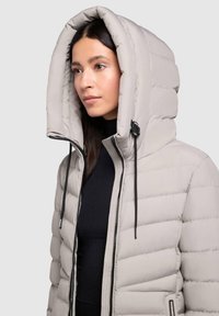 Gevoerde lichtgrijze jas met een oversized capuchon, ritssluiting aan de voorkant, verstelbare trekkoorden en een gewatteerde textuur.