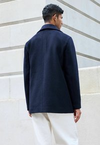 Abrigo de mezcla de lana en color navy, con un cuello estructurado, mangas largas y corte recto, que presenta una textura suave y detalles de costura mínimos.