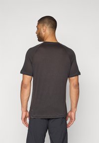 Schwarzes T-Shirt mit kurzen Ärmeln, gerippter Textur und Raglanärmeln, mit einem geraden Schnitt und einem kleinen Logoakzent nahe dem Saum.