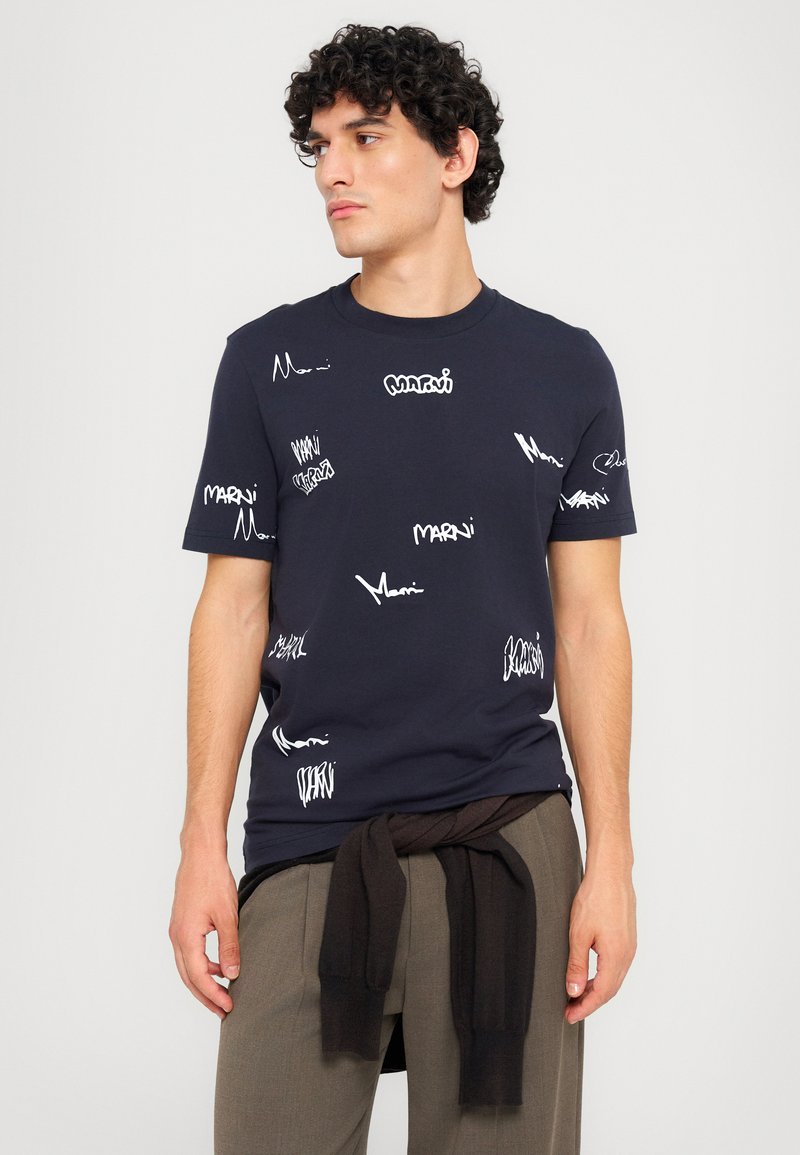 Camiseta de algodón azul marino con texto gráfico en blanco y patrones por toda la prenda. Manga corta, cuello redondo, corte relajado y textura suave.