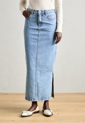 Lys blå denim maxi-skjørt med splitt foran, høy midje og baklommer. Brukes med hvite, flate sko med bue-detaljer.