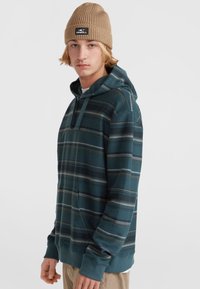 Teal gestreepte hoodie met een zachte textuur, voorzien van een voorvak en een capuchon met trekkoord. Gecombineerd met een tan ribbelige beanie.