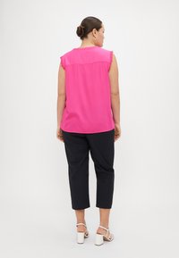 Top rosa senza maniche con dettagli a volant, abbinato a pantaloni neri 3/4. L'outfit è completato da sandali bianchi con tacco a blocco.