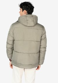 Giacca puffer di colore grigio chiaro, presenta un cappuccio, polsini a coste e un design trapuntato orizzontale. Superficie texture con finitura liscia.