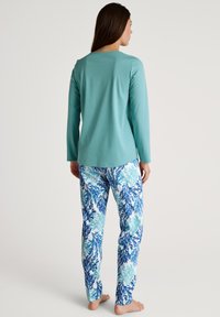 Helles türkisfarbenes Langarmshirt kombiniert mit gemusterten Hosen, die blaue und aquafarbene Seegrasdesigns auf weißem Hintergrund zeigen. Weicher Stoff.