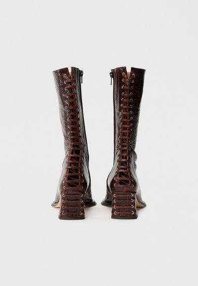 Καφέ δερμάτινες μπότες έως το γόνατο με κορδόνια μπροστά, πλευρικά φερμουάρ και χοντρούς τακούνια με υφή.