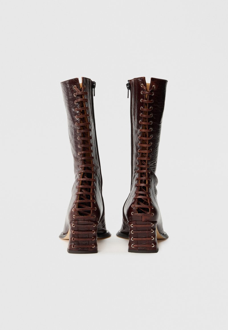 Bruine leren kniehoge laarzen met een vetersluiting aan de voorkant, ritsen aan de zijkant en chunky hakken met een structuur.