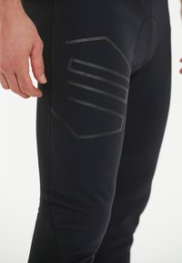 Svarta sportleggings med en matt svart texturerad logotyp på låret. Slät tyg med en figurnära design och elastisk midjeband.