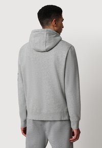 Felpa grigia con cappuccio regolabile, polsini e vita a coste. Tessuto morbido e strutturato con una vestibilità rilassata, indossata con pantaloni della tuta grigi coordinati.