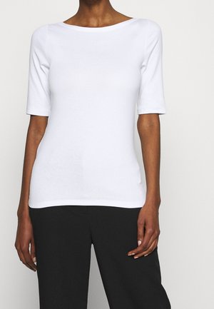 Valkoinen pusero, jossa on lyhyet hihat ja leveä pääntie, tehty sileästä kankaasta, yhdistetty mustiin housuihin. Malli on vartalonmyötäinen ja sivuilla on halkiot.