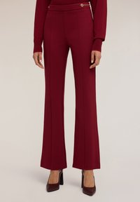 Bordeauxkleurige flared broek met een zachte textuur, voorzien van zijnaaddetails en een decoratieve hardwareaccent in goudkleur op de tailleband.