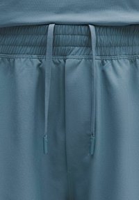 Vaaleansiniset urheilushortsit, joissa on joustava vyötärönauha kiristysnaruilla, sileä pinta ja hienovaraiset ompelu- ja yksityiskohdat.