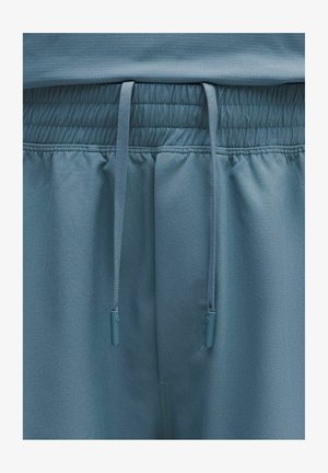 Vaaleansiniset urheilushortsit, joissa on joustava vyötärönauha kiristysnaruilla, sileä pinta ja hienovaraiset ompelu- ja yksityiskohdat.