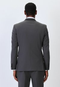 Chaqueta de traje gris con tejido texturizado. Presenta un corte entallado, solapas con muesca, un solo respiradero y puños de cuatro botones. La vista trasera muestra un diseño entallado.