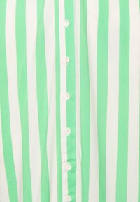 Grün-weiße gestreifte Baumwollbluse mit einer Knopfleiste an der Vorderseite, die kleine weiße Knöpfe zeigt, die vertikal über den Stoff verlaufen.