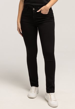 Czarne obcisłe jeansy z denimu z wysokim stanem, wyposażone w zapięcie na guziki z przodu oraz boczne kieszenie. Połączone z białymi trampkami.
