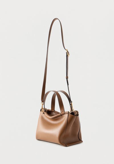 Barna bőrből készült kézitáska, két rövid füllel és egy állítható hosszú vállpánttal, világos háttéren pihenve.